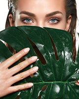 Schöne dunkelhaarige Frau mit blauen Augen mit Palmen Blatt vor dem Gesicht. Werbegesicht von dem Relax-Cottage